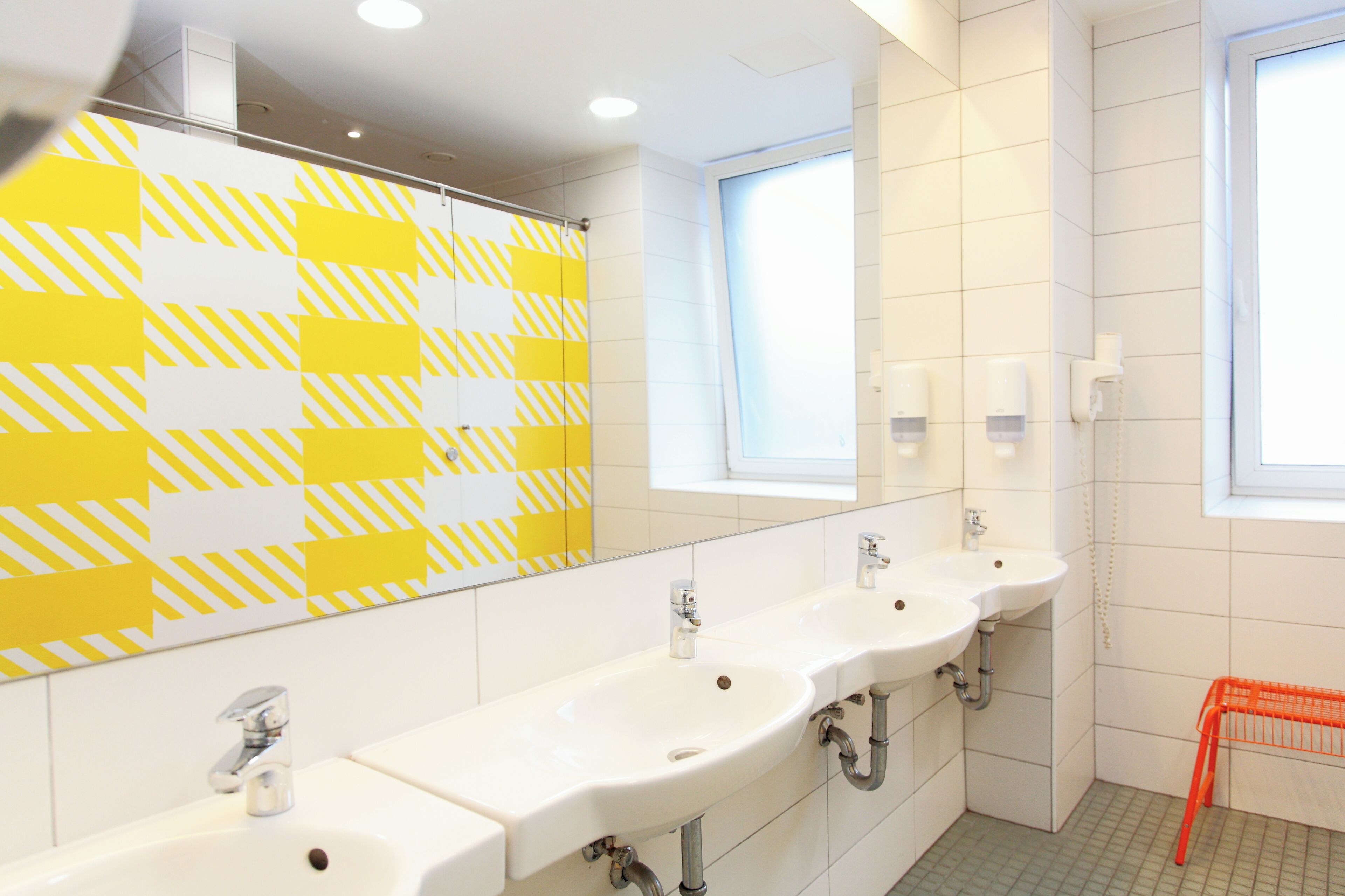 A modern bathroom with three sinks, a mirror, and a window.