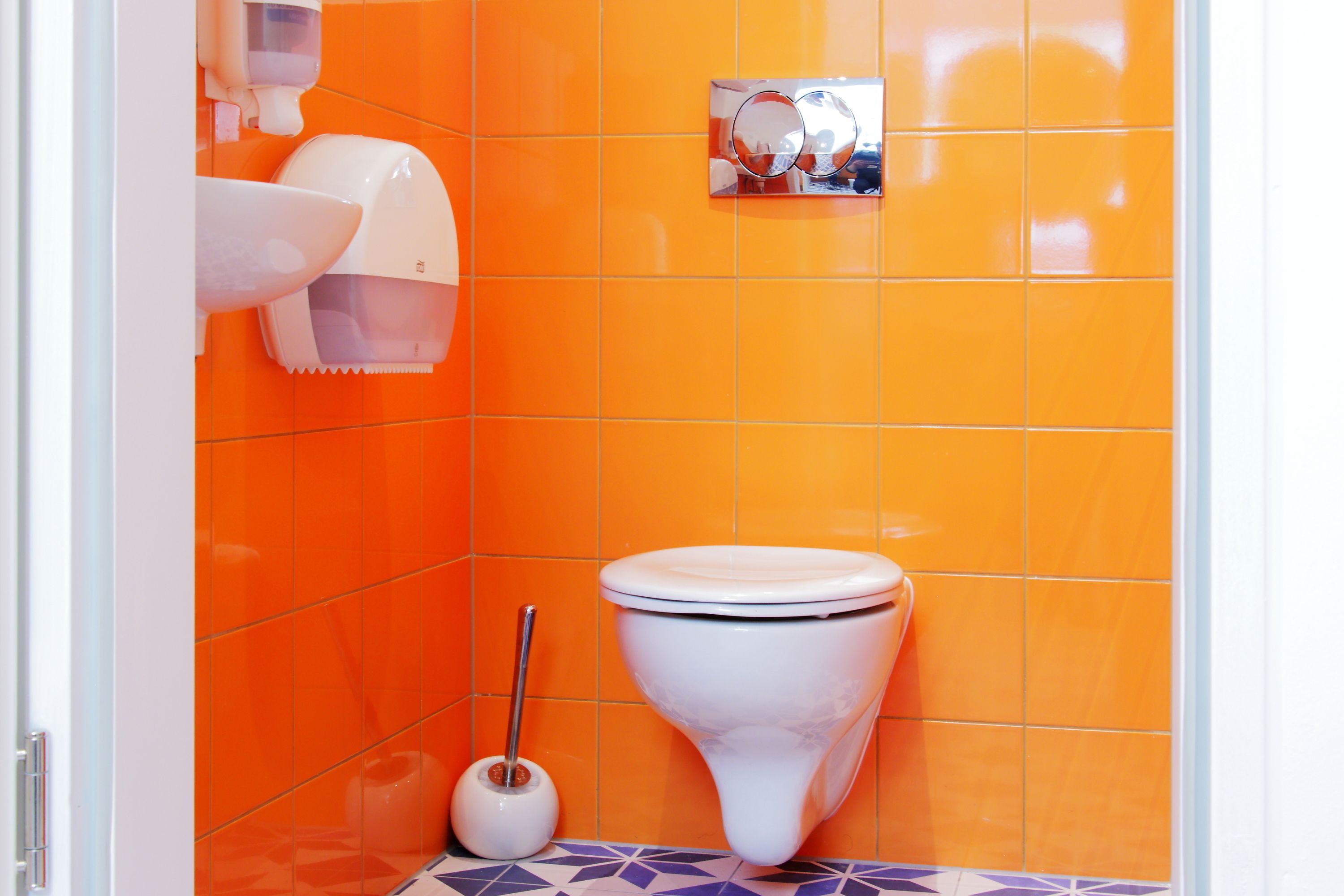 Un bagno con una parete piastrellata arancione, un water bianco e un asciugamani ad aria.