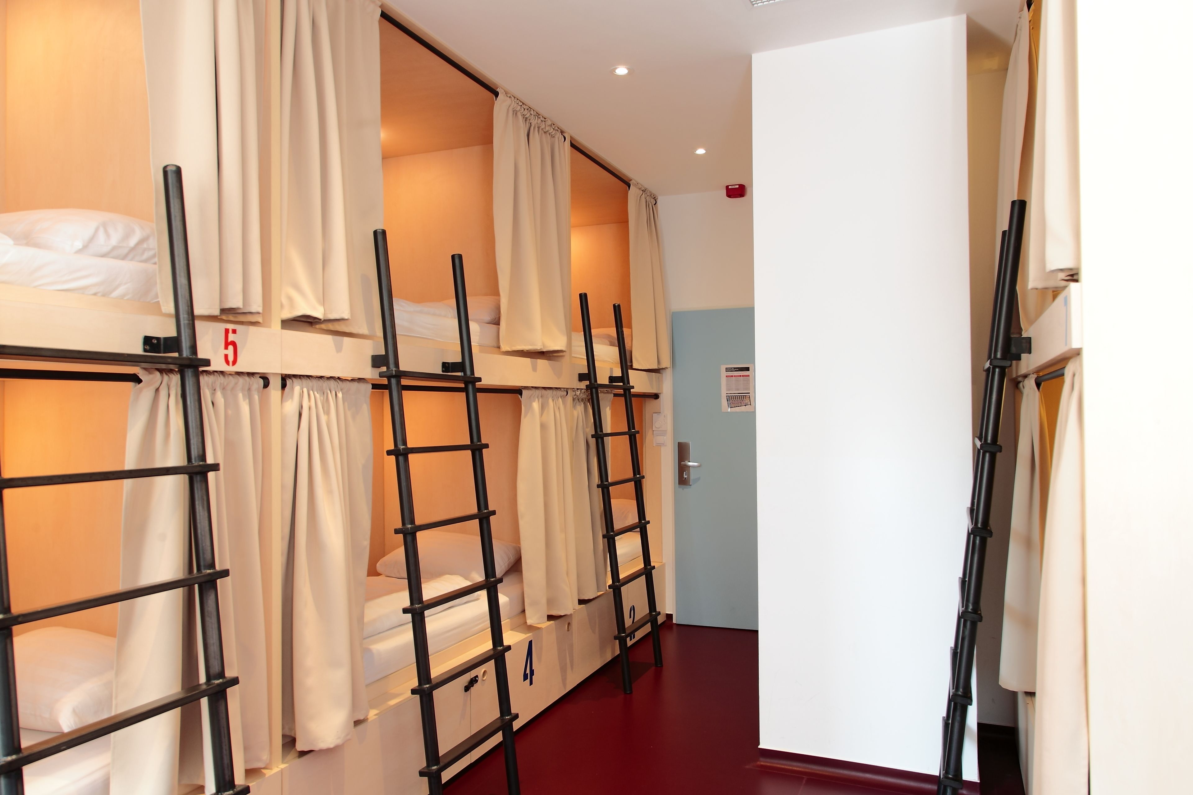 A dormitory room with bunk beds, numbered beds, and a door to another room.