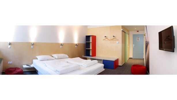 Hotellihuoneessa on sänky, punainen papupussi, pieni pöytä ja seinälle asennettu televisio.