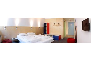 Een hotelkamer met een bed, een rode relaxfauteuil, een klein tafeltje en een aan de muur bevestigde televisie.