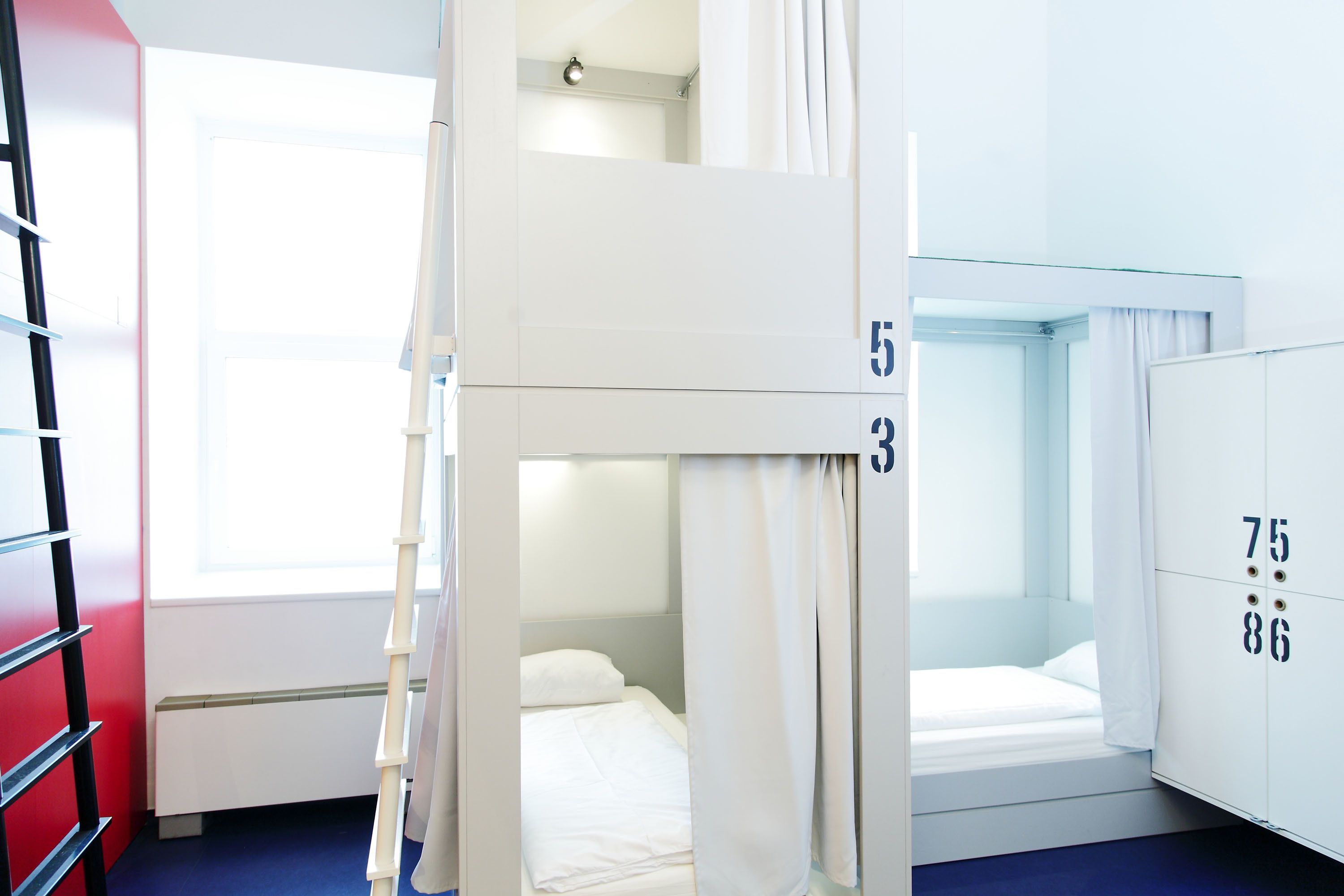 Quarto com beliche, janela, guarda-roupa branco com números e parede vermelha.