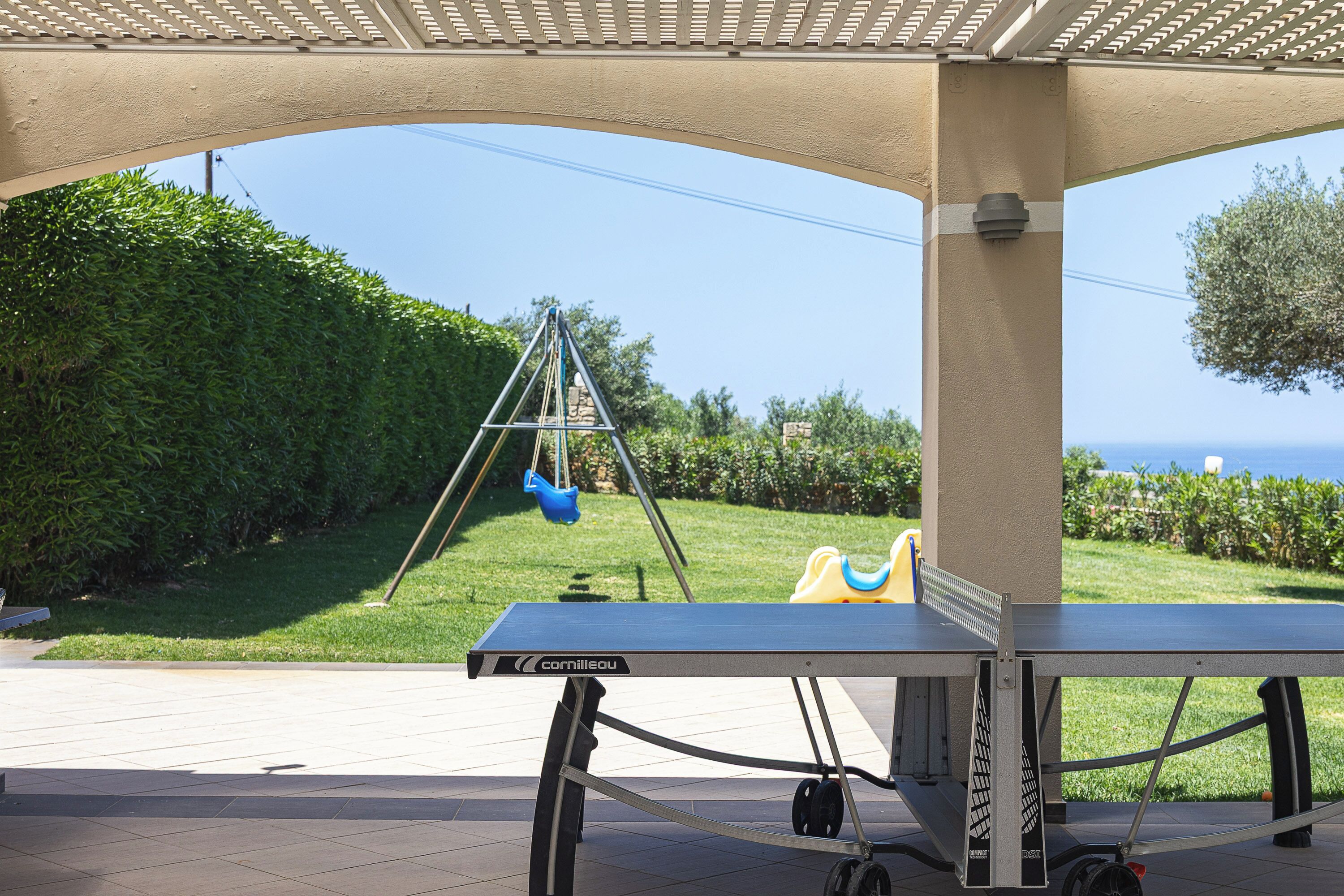 A covered outdoor area with a table tennis table, a swing set, and a view of the sea.