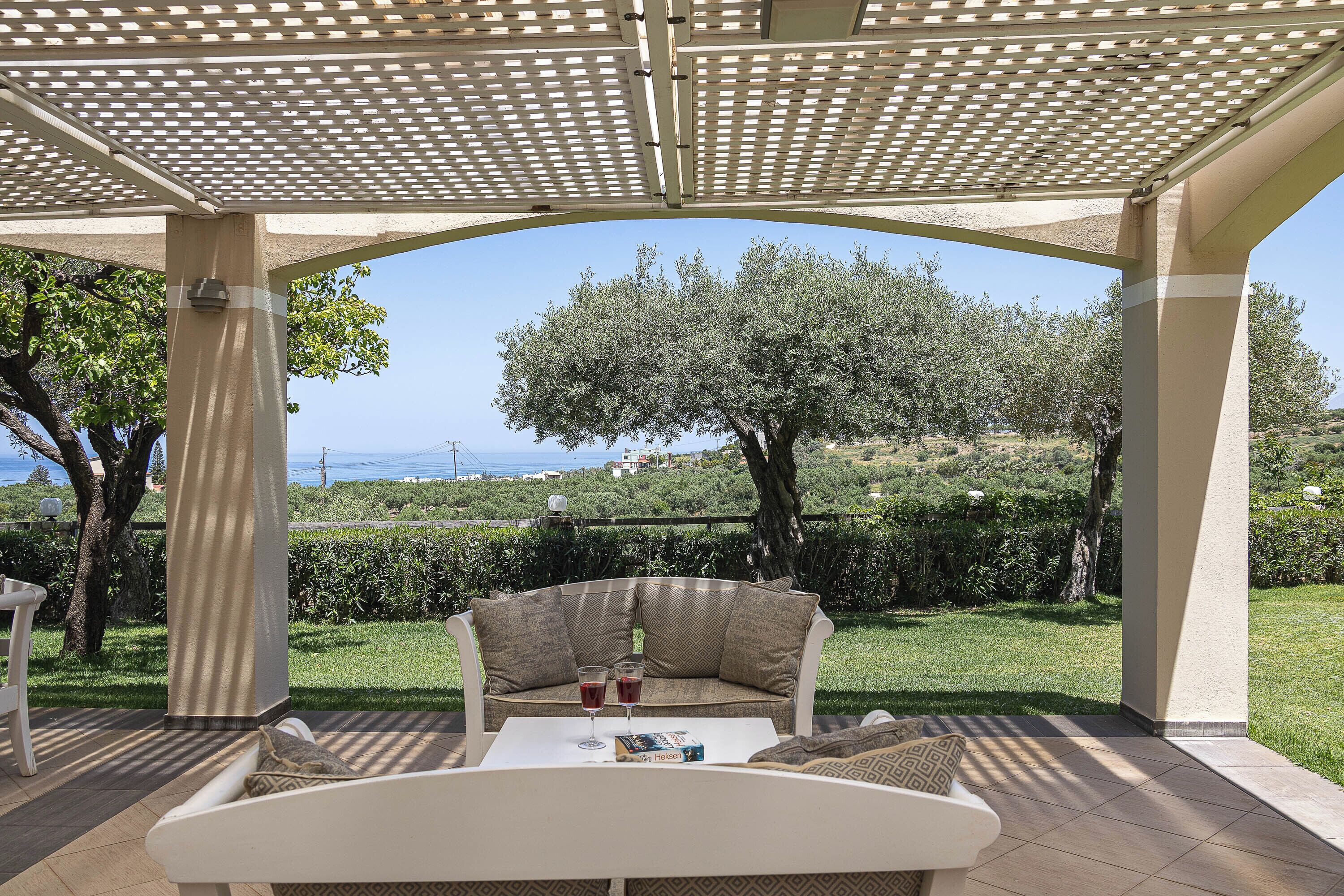 An outdoor seating area with a pergola, a cushioned bench, and a table with drinks.