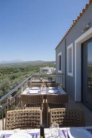 A balcony with wicker furniture, a table set for dining, and a view of the landscape. - Carme Villas (Rethymno)