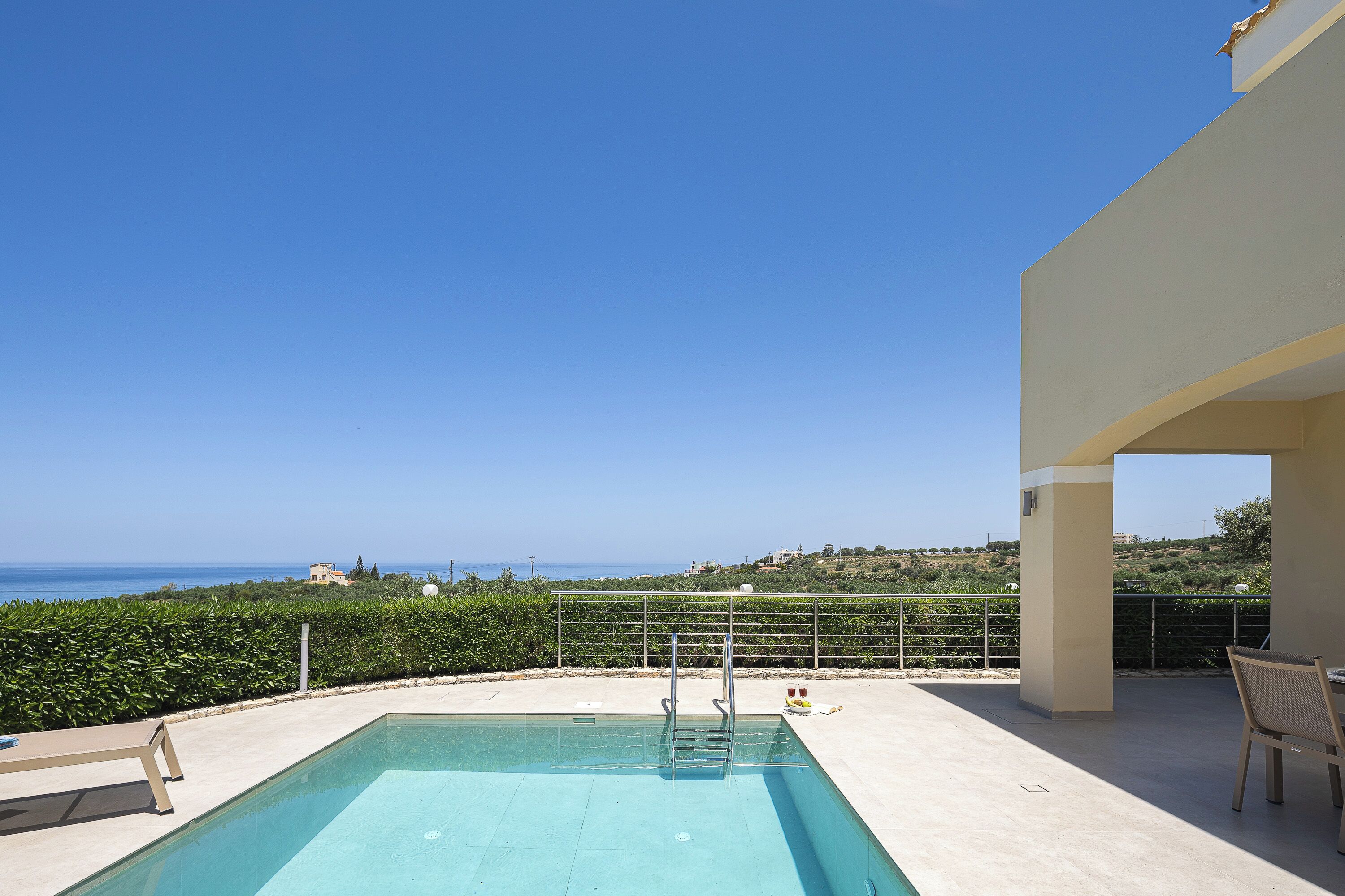 A swimming pool with a view of the sea, a covered patio area, and a table with chairs.