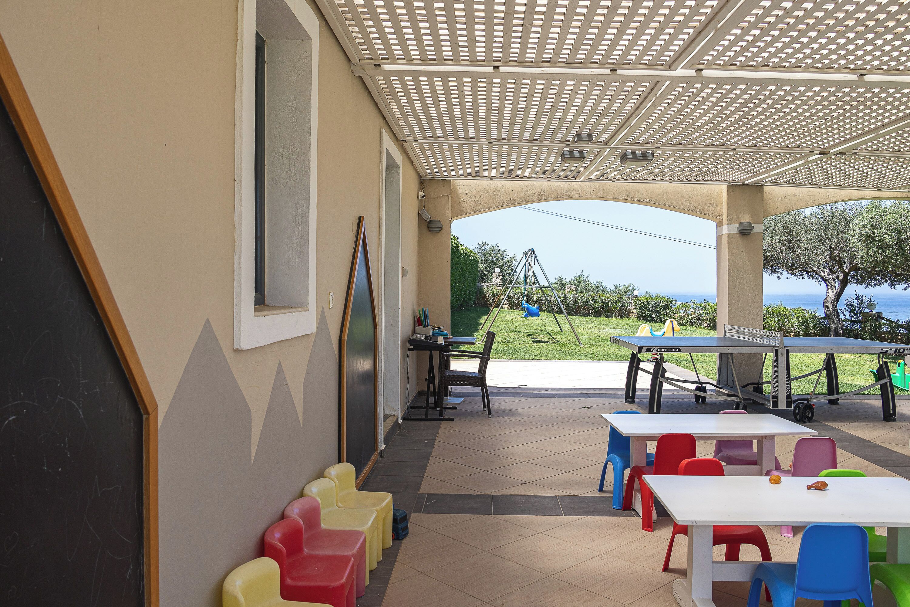 A covered outdoor area with tables and chairs, a chalkboard, and a view of the sea.