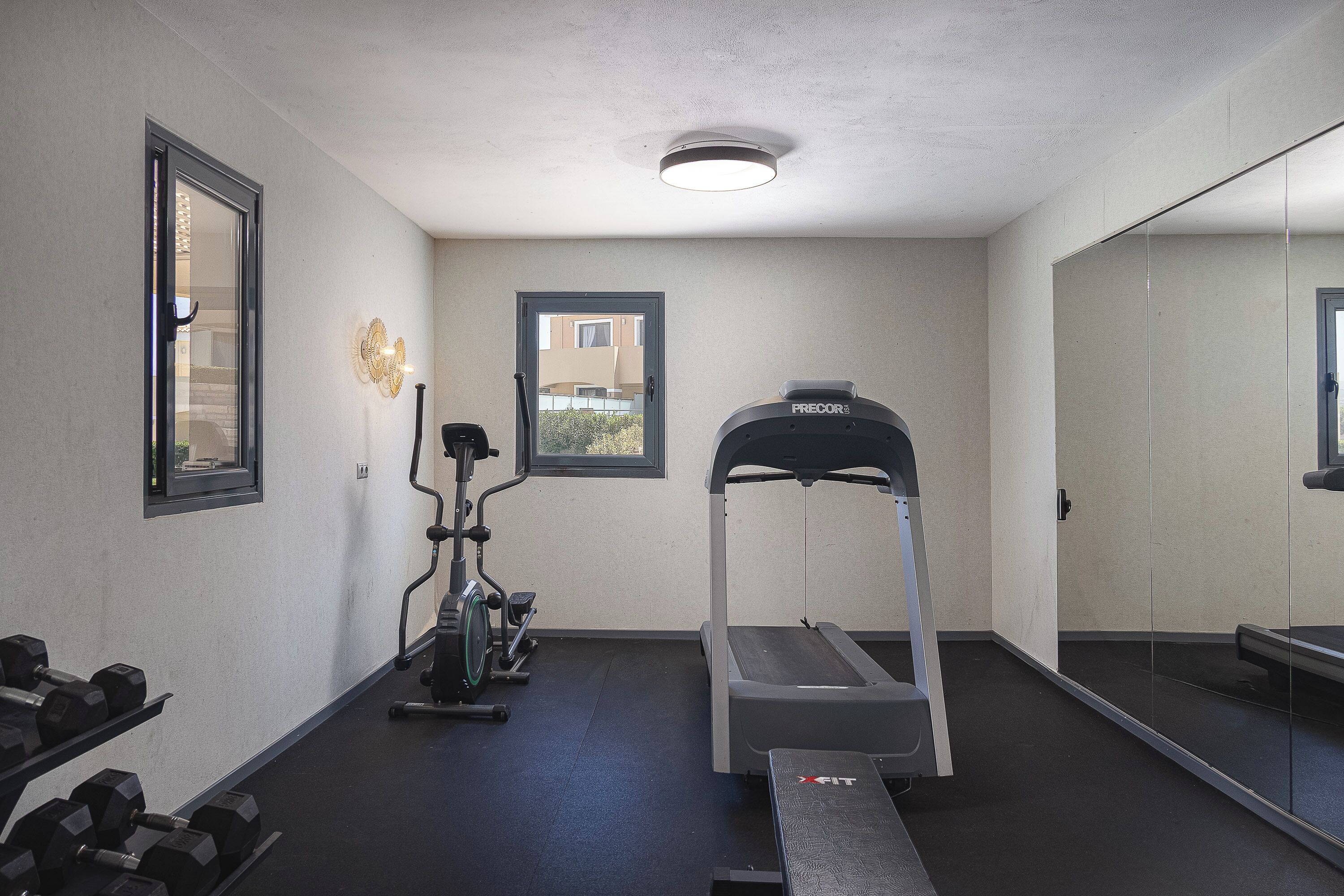 Ein Fitnessstudio mit Laufband, Crosstrainer und Kurzhanteln.