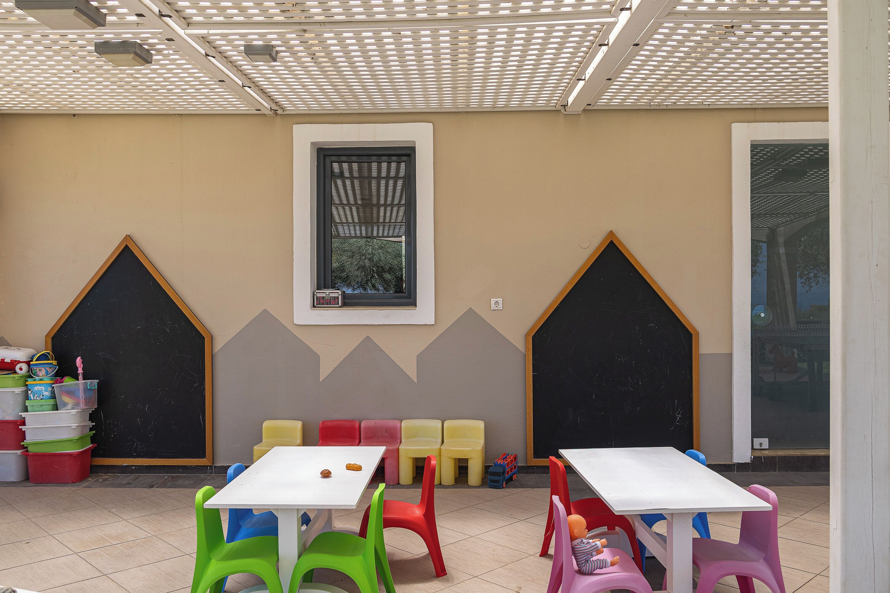 Een kinderspeelruimte met tafels, stoelen, een schoolbord en opbergbakken.
