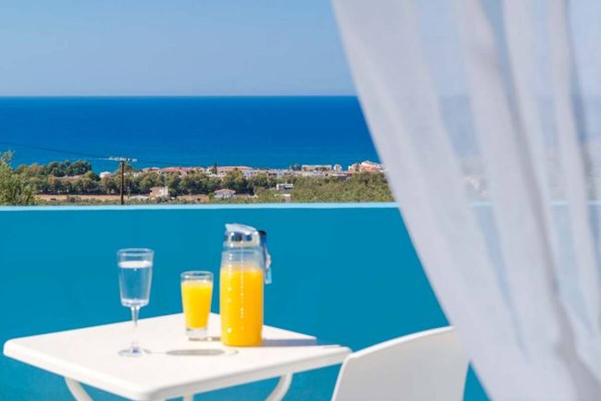 A table with two glasses and a pitcher of orange juice, overlooking a coastal town.
