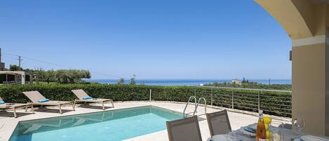 A poolside area with lounge chairs, a dining table set for two, and a view of the sea.