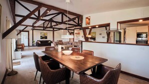 A spacious dining area with a wooden table and leather chairs, a high ceiling with exposed beams, and a kitchen area with modern appliances. - Askegaarden Apartments (Sandved)