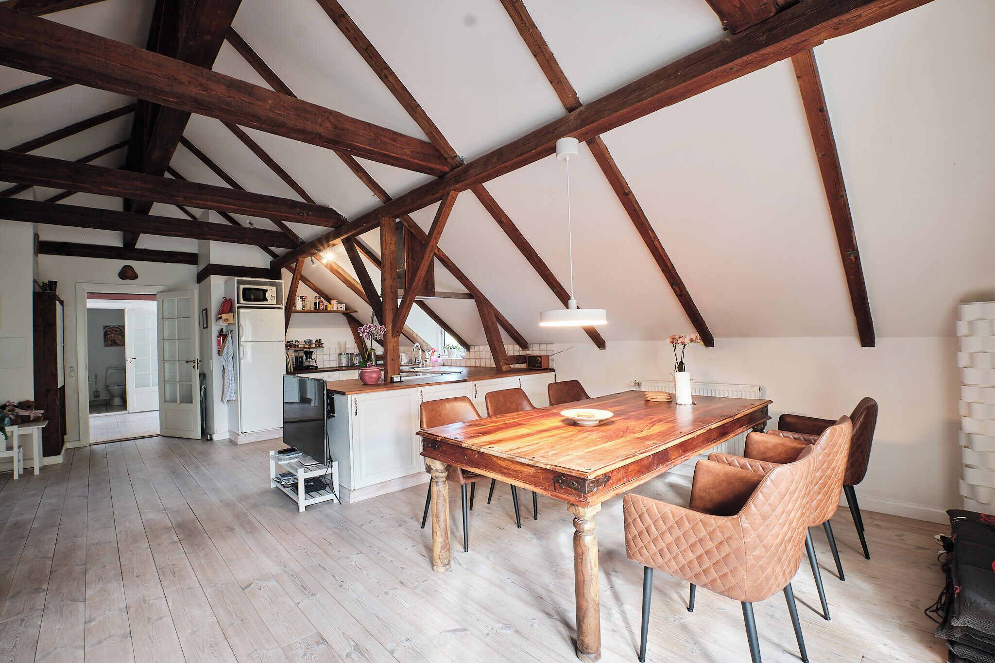 A spacious loft with exposed wooden beams, a large wooden dining table, and modern leather chairs.