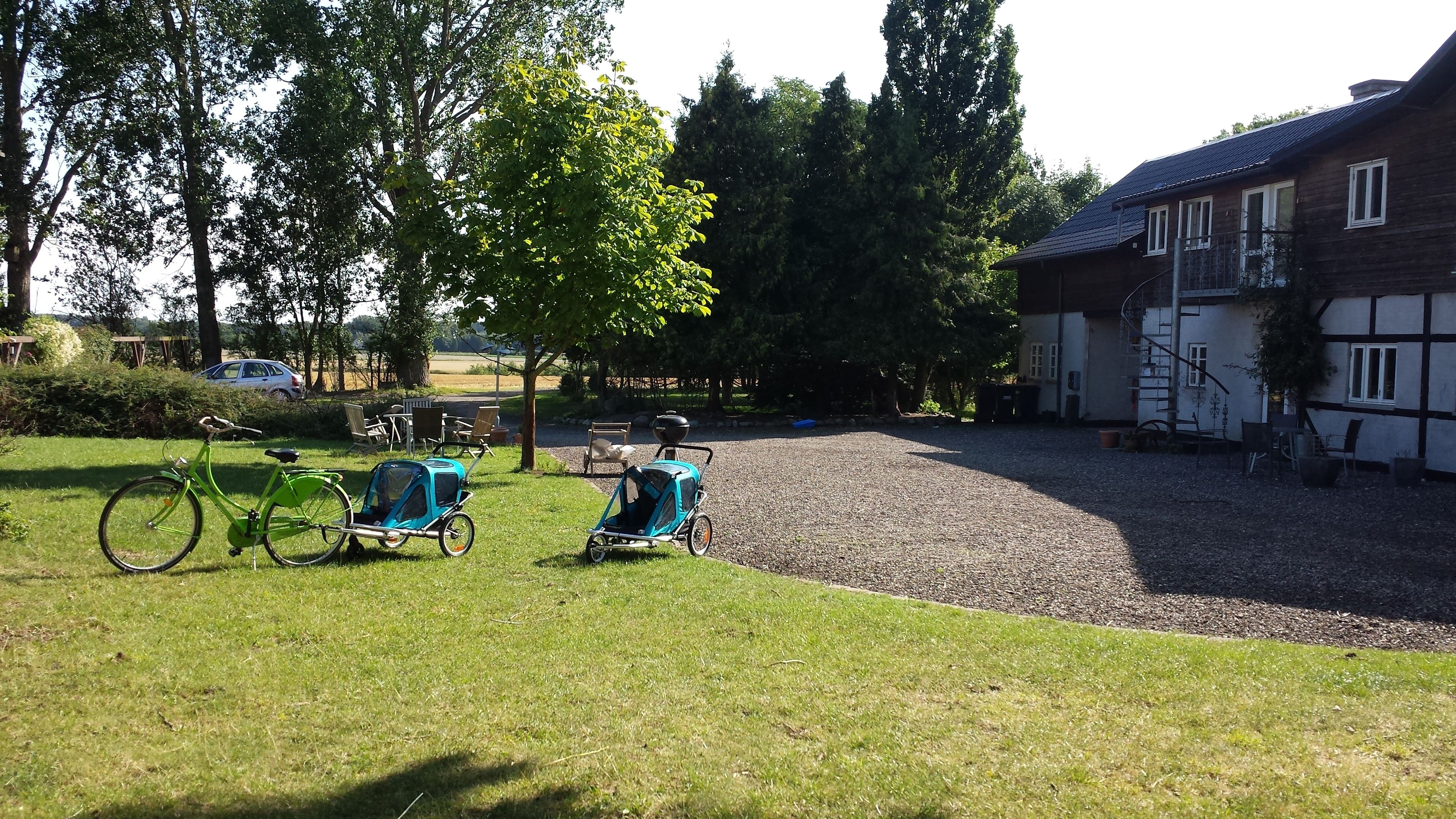 A grassy area with two strollers, a bicycle, and a building with a sloped roof.