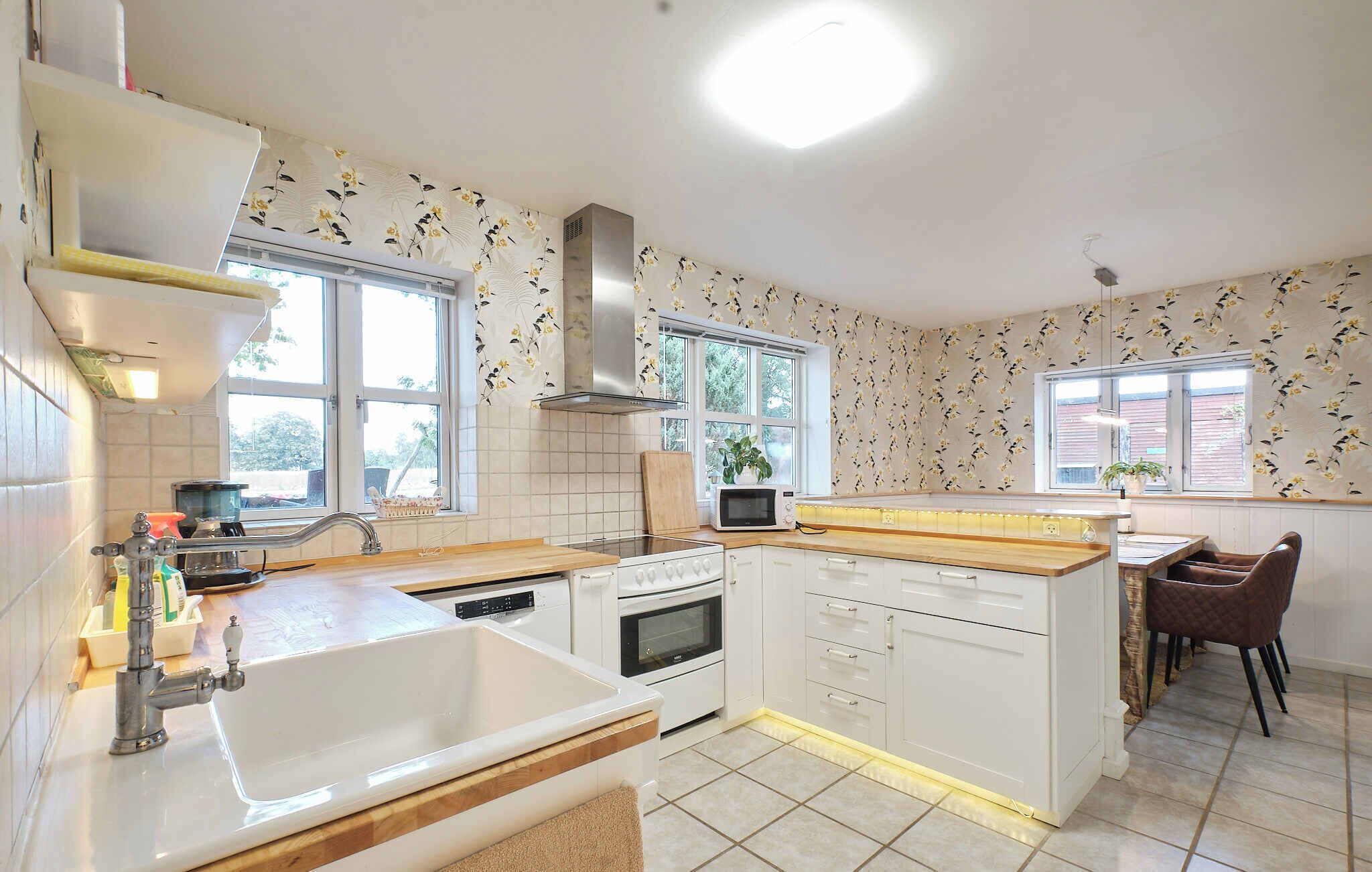 A modern kitchen with white cabinetry, a built-in oven, a microwave, and a large window providing natural light.