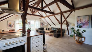 A spacious loft with exposed wooden beams, a kitchen with a stove, a dining area, and a living room with a sofa and a coffee table. - Askegaarden Apartments (Sandved)