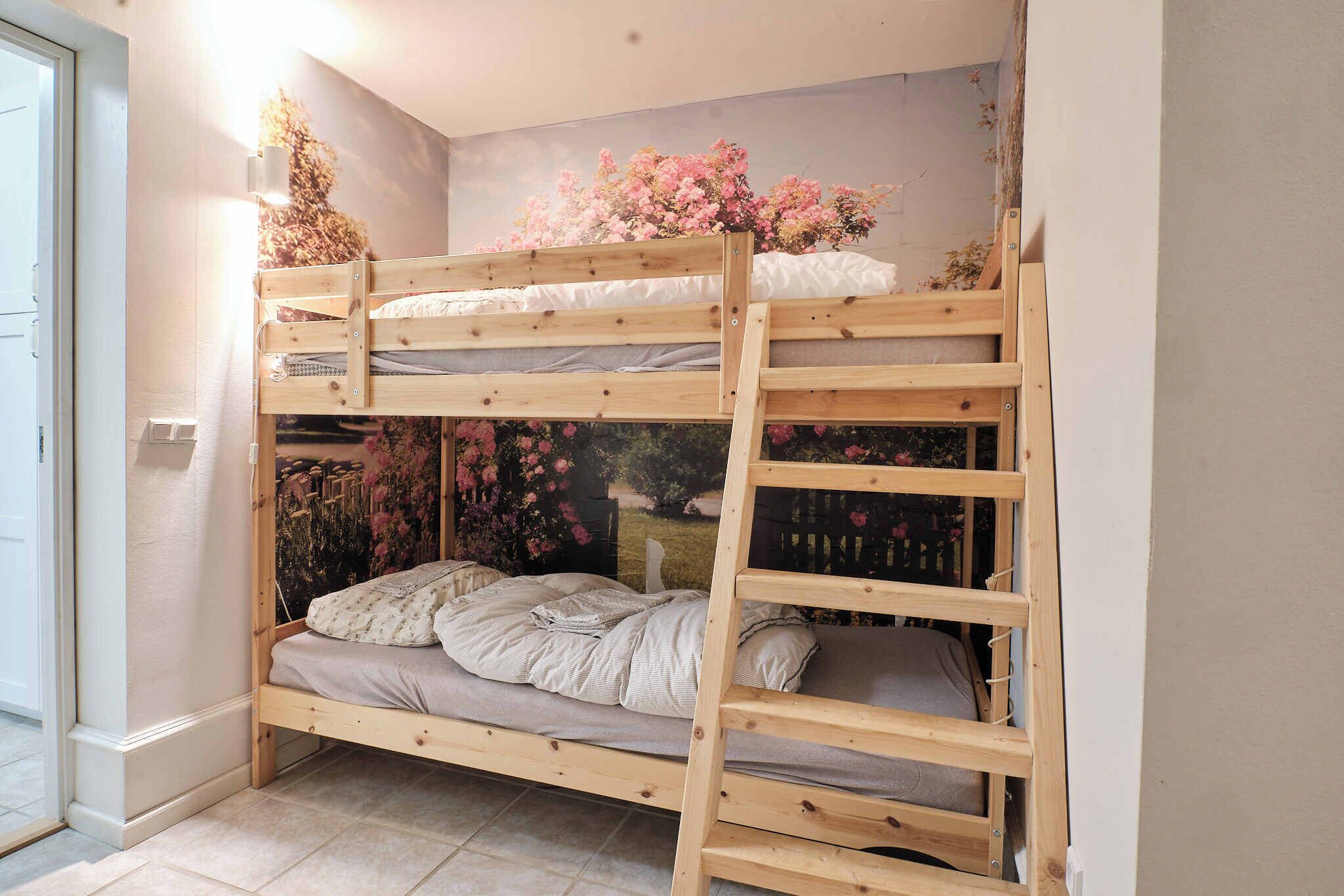 A bunk bed with a wooden ladder, a floral wall decoration, and a window with a view of a garden.