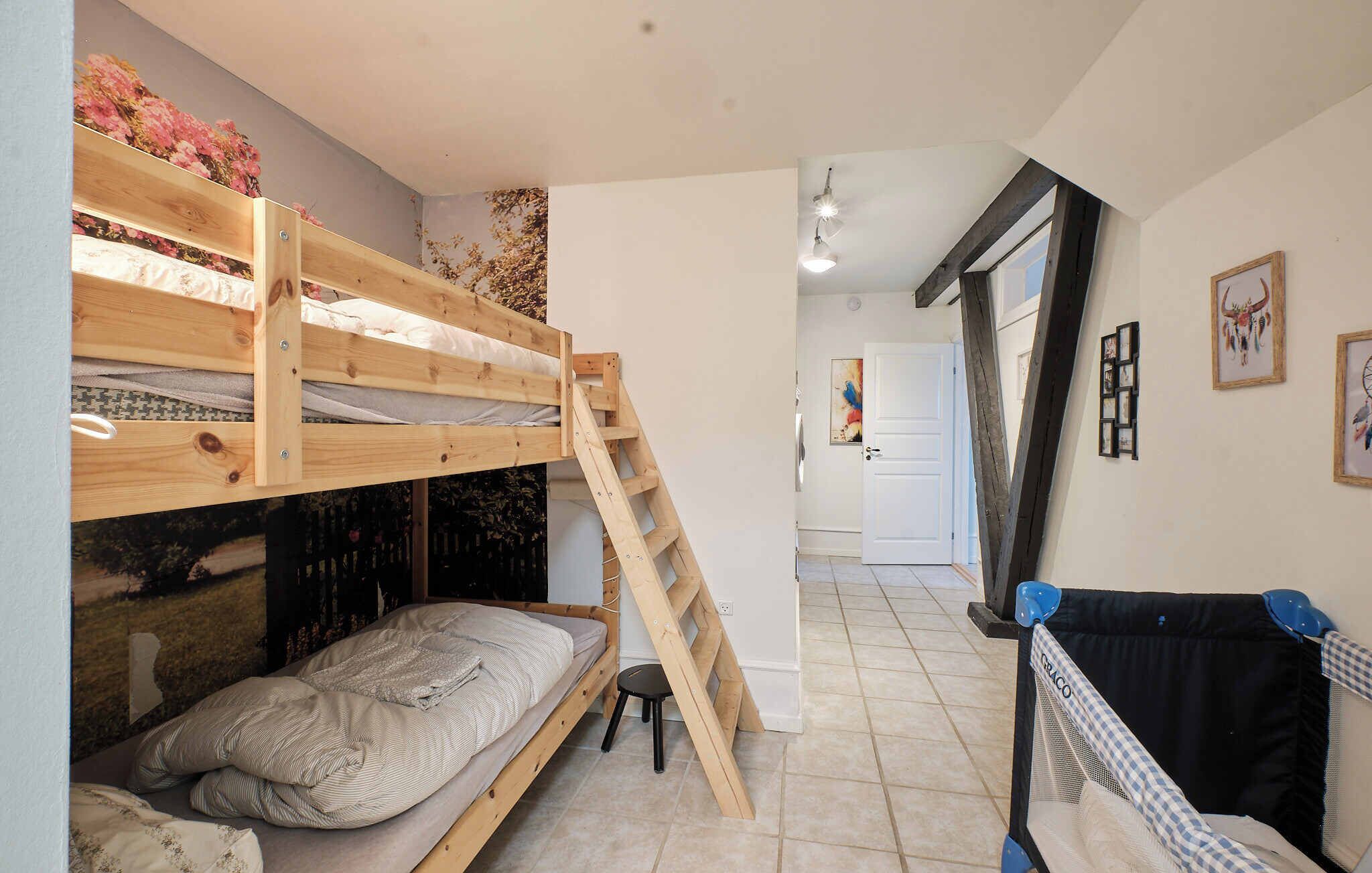 Une chambre avec un lit superposé, une échelle, un petit tabouret et un berceau.