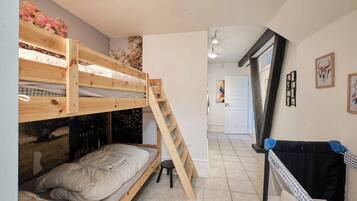 Une chambre avec un lit superposé, une échelle, un petit tabouret et un berceau.