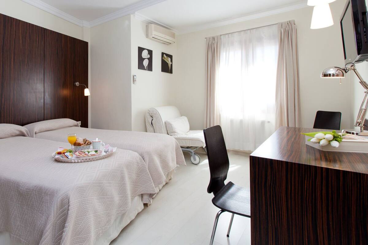 A hotel room with two beds, a desk, and a chair. There is a tray with breakfast items on one of the beds.