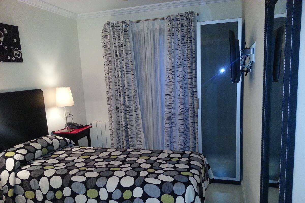 A hotel room with a bed, a nightstand, a lamp, a telephone, and a television.