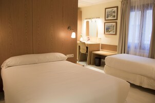 A hotel room with two beds, a desk, a chair, a mirror, and a window with curtains.