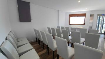 Un salón de conferencias con filas de sillas, una pantalla de proyector y una ventana con vistas a la ciudad.