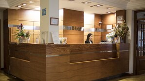 Un mostrador de recepción con detalles de madera, un letrero que dice "m&Hotel Costa Rica" y una recepcionista.