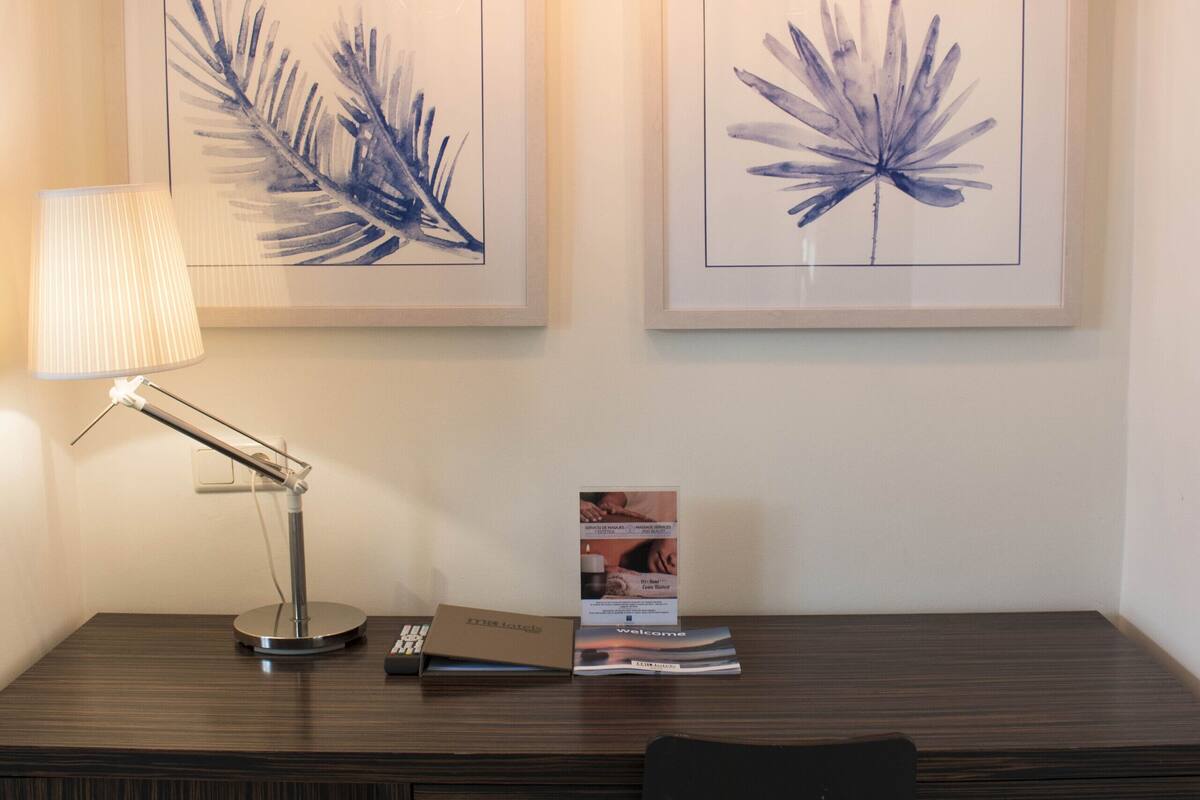 A modern desk with a lamp, framed artwork, and a chair.
