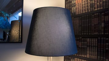 A lamp with a textured shade, a bookshelf with books, and a wall with a mirror.
