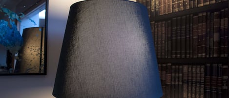 A lamp with a textured shade, a bookshelf with books, and a wall with a mirror.