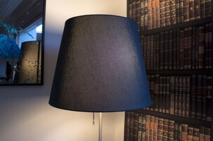 A lamp with a textured shade, a bookshelf with books, and a wall with a mirror.