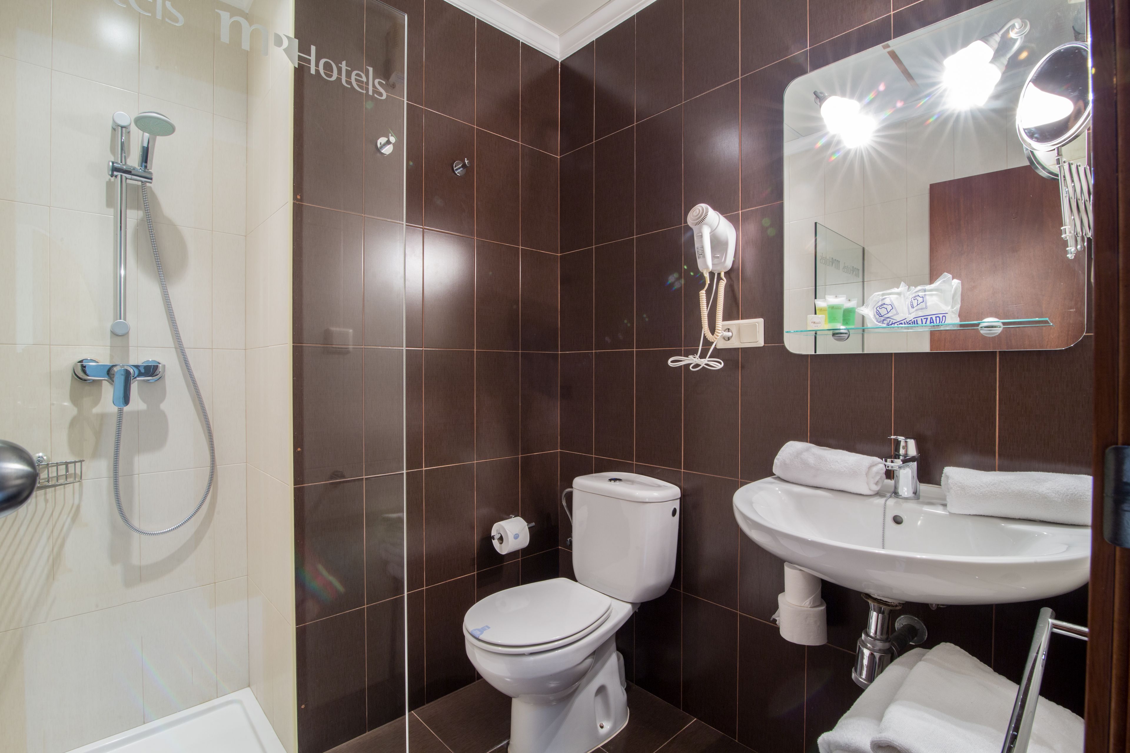 A modern bathroom with a shower, toilet, sink, and a mirror with lights.
