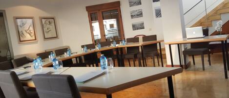 A conference room with a long table, chairs, and water bottles. There are framed pictures on the wall and a staircase in the background.