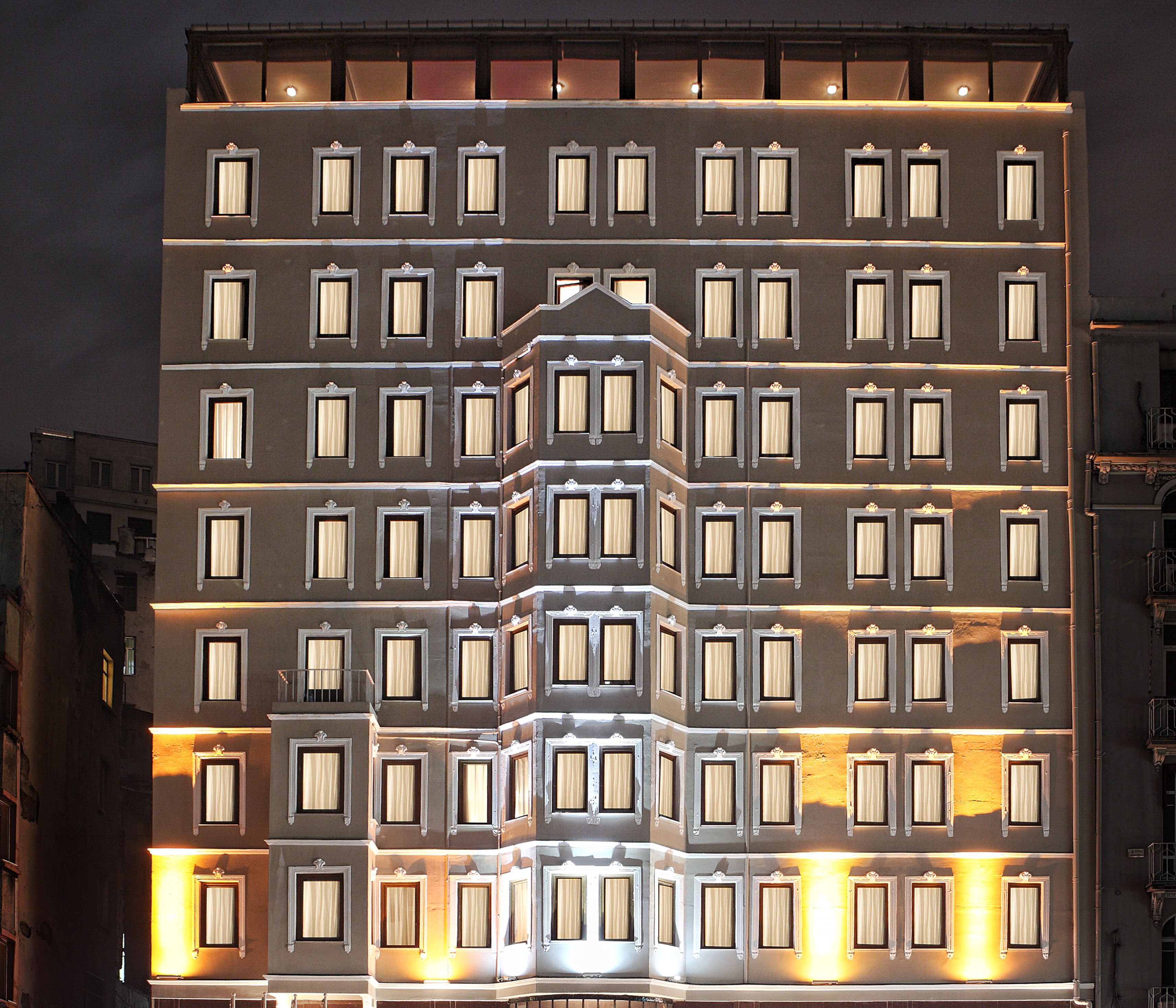 Un hôtel à plusieurs étages, doté d’une façade symétrique, de fenêtres régulièrement espacées et d’une entrée centrale surmontée d’une arche décorative.