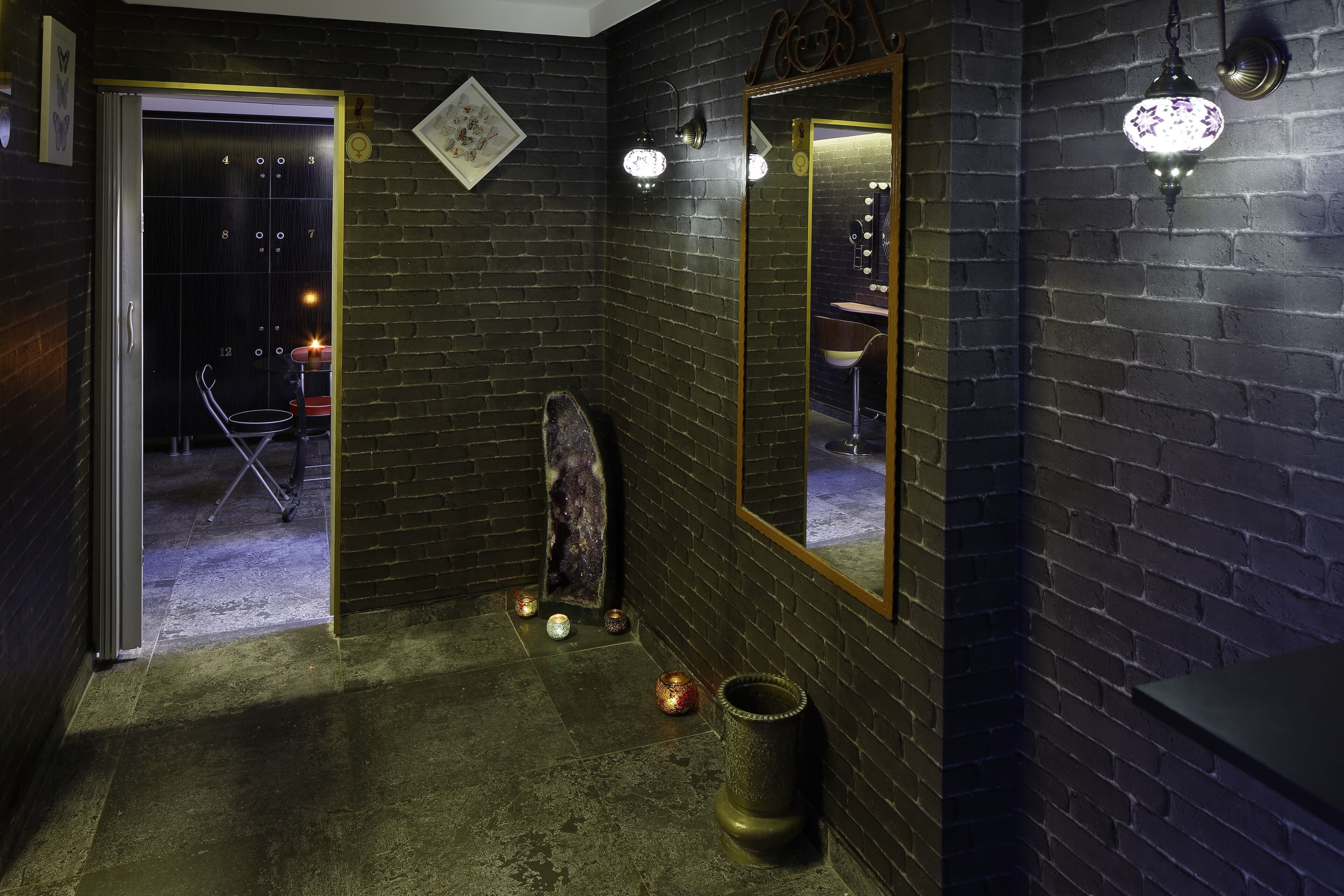 A dark brick-walled bathroom with a mirror, a sink, and a small seating area.