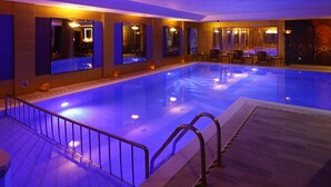 A large indoor swimming pool with a glass barrier, multiple seating areas, and a view of the pool through large windows.