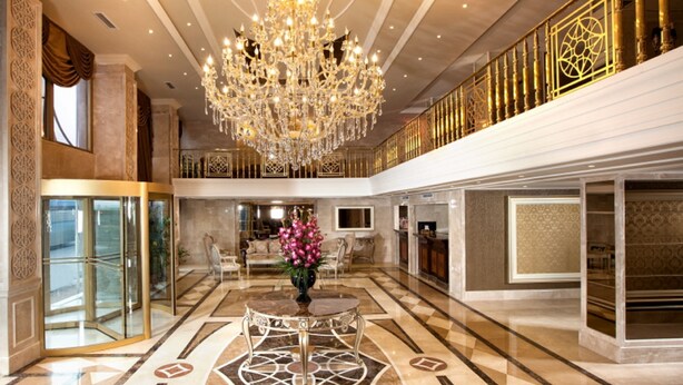 A luxurious lobby with a grand chandelier, marble flooring, and a central seating area.
