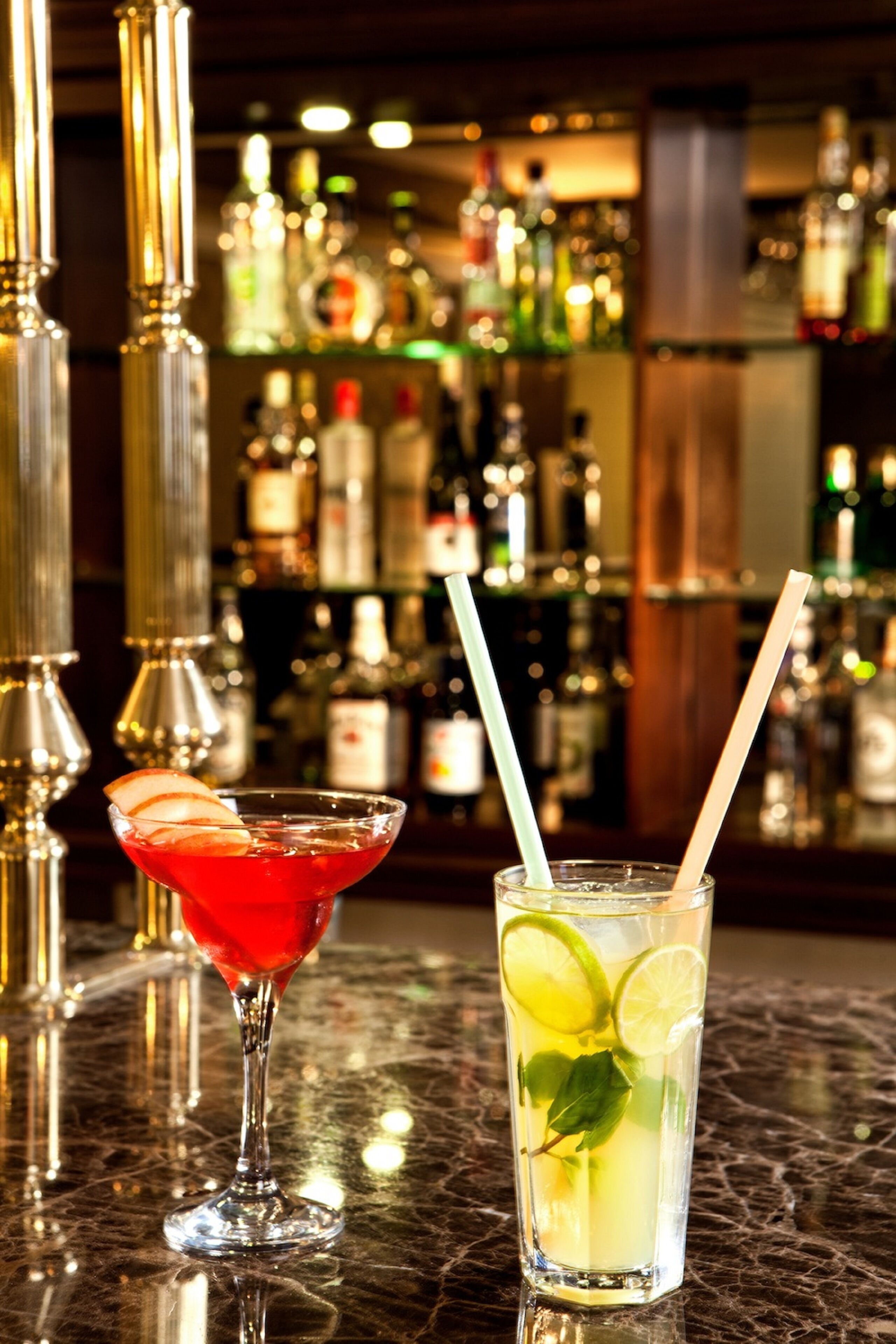 Two drinks on a bar counter with a blurred background of bottles.