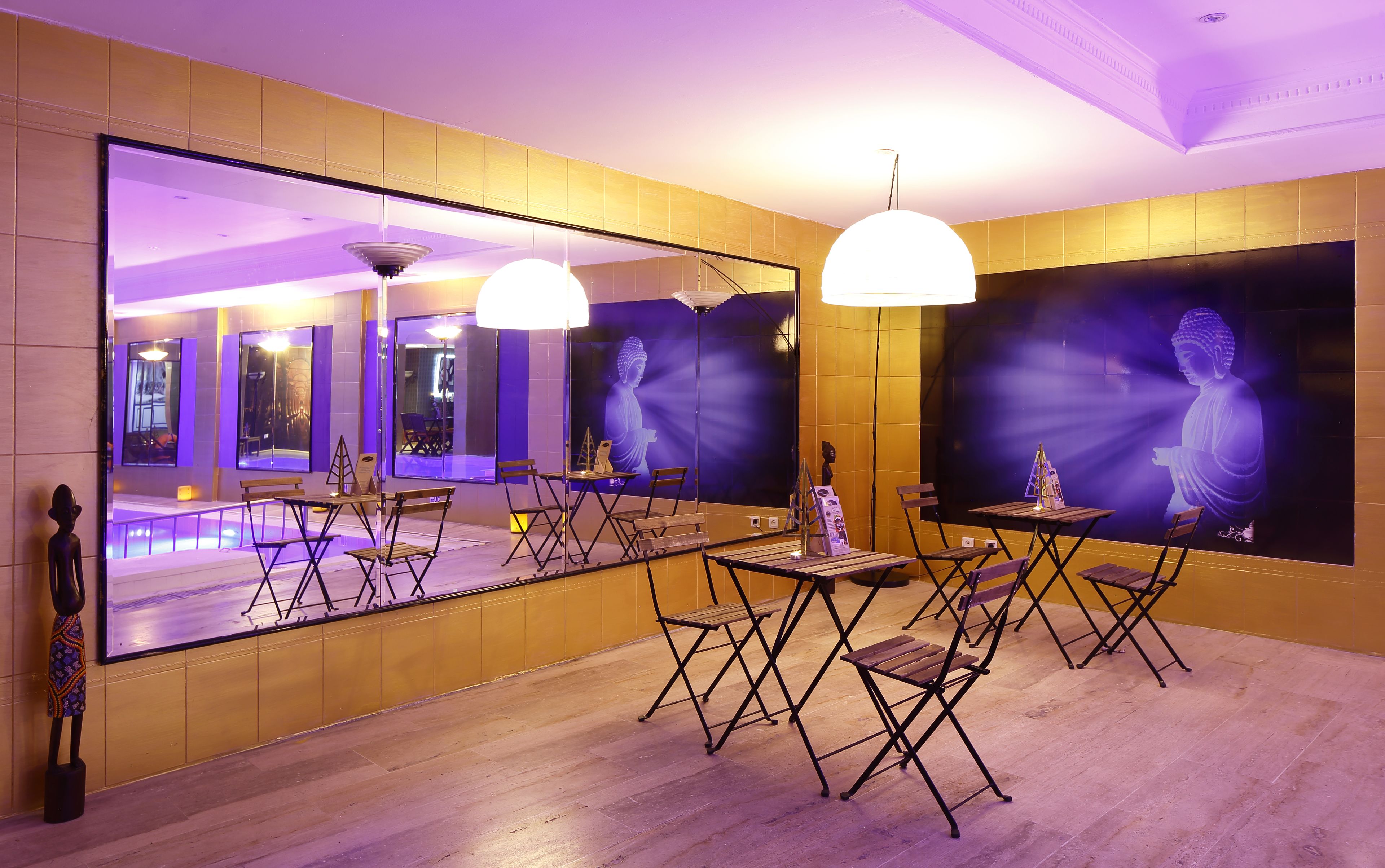 Een kamer met een grote spiegel die een Boeddhabeeld reflecteert, en een kamer met een houten vloer en opklapbare stoelen.