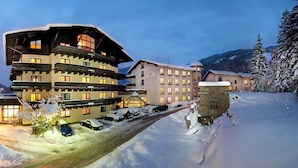 Ein mehrstöckiges Hotel mit verschneiter Fassade, einer Seilbahn im Hintergrund und freiem Blick auf die umliegenden Berge.