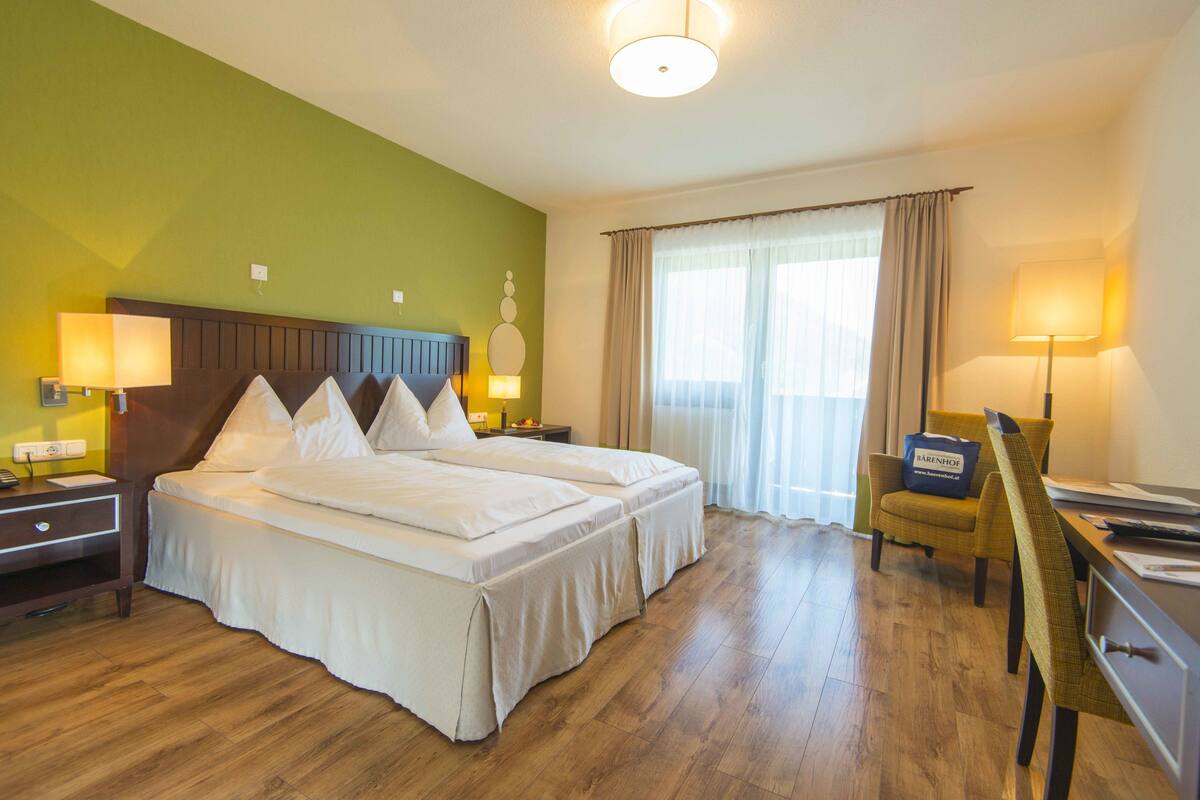 A hotel room with a large bed, a desk, a chair, and a window with curtains.