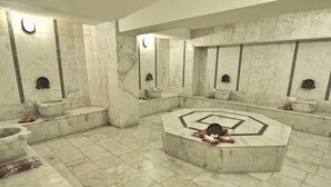 Une salle de bain au sol en marbre, dotée de plusieurs lavabos et d’un espace salon central.
