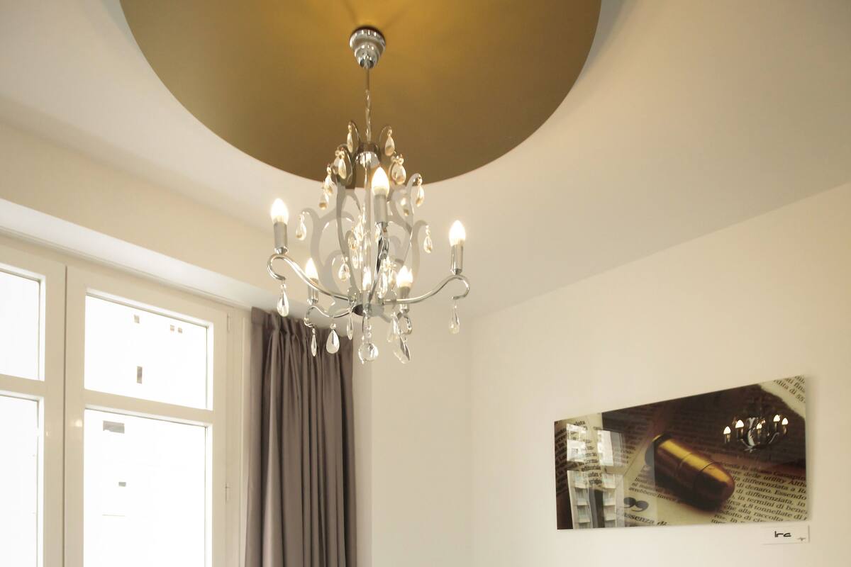 Quarto com uma cama grande, um candelabro, janela com cortinas e uma obra de arte pendurada na parede.