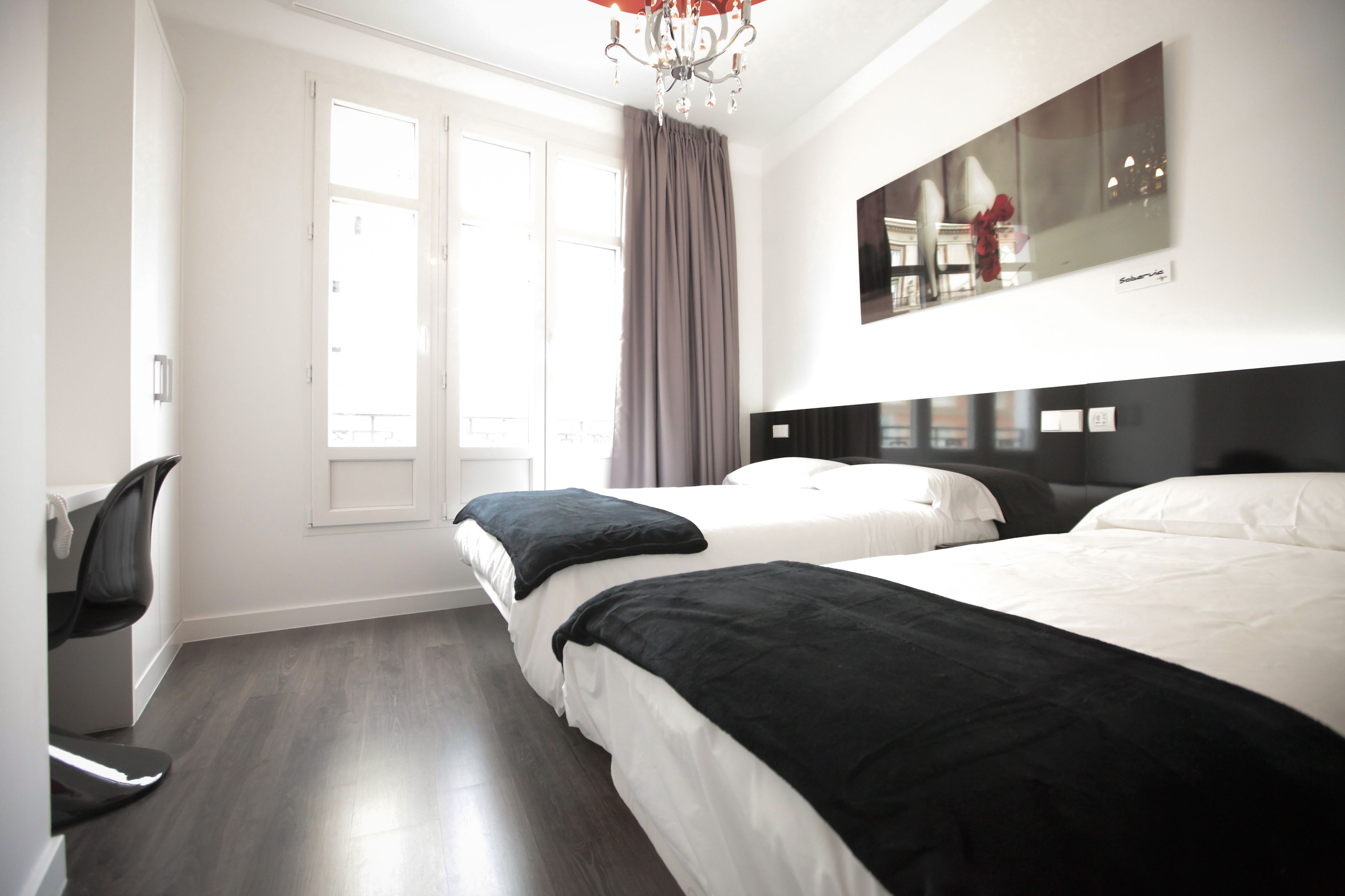 A hotel room with two beds, a large mirror, a chandelier, and a view of the city through the window.
