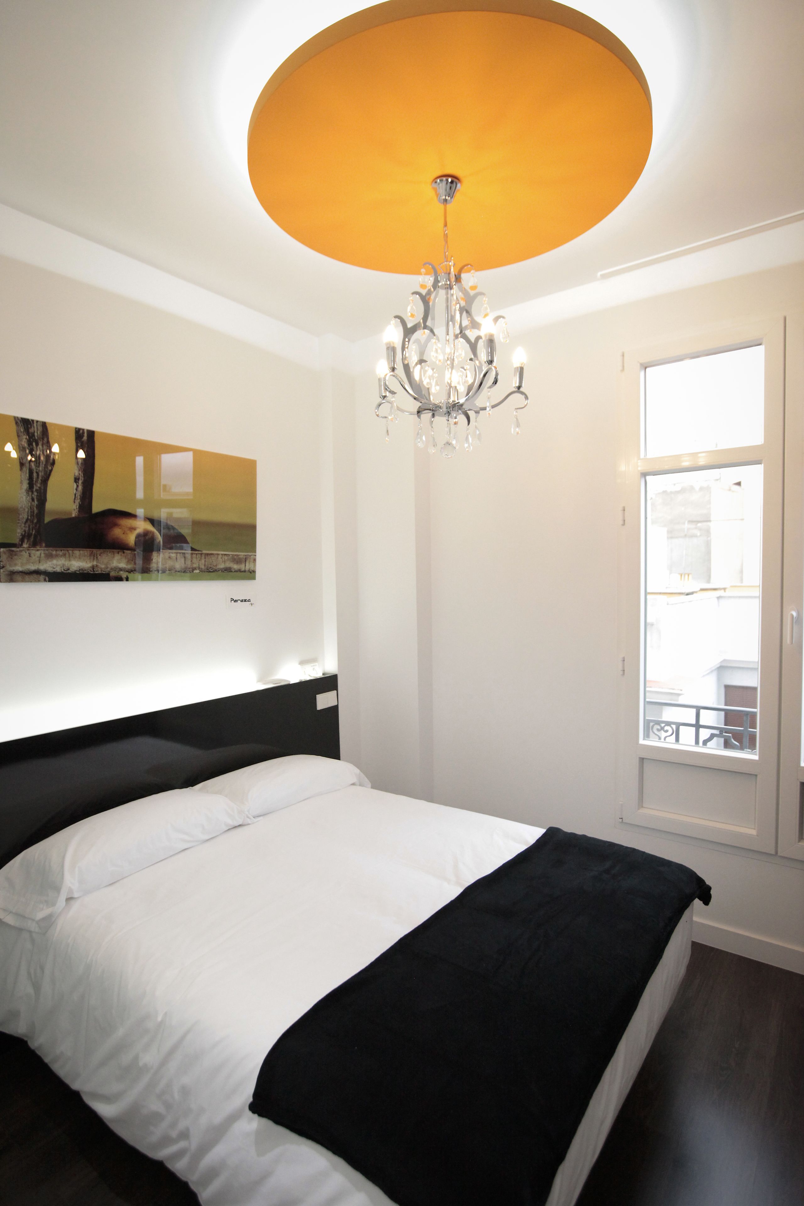 A bedroom with a large bed, a chandelier, a window, and a painting on the wall.