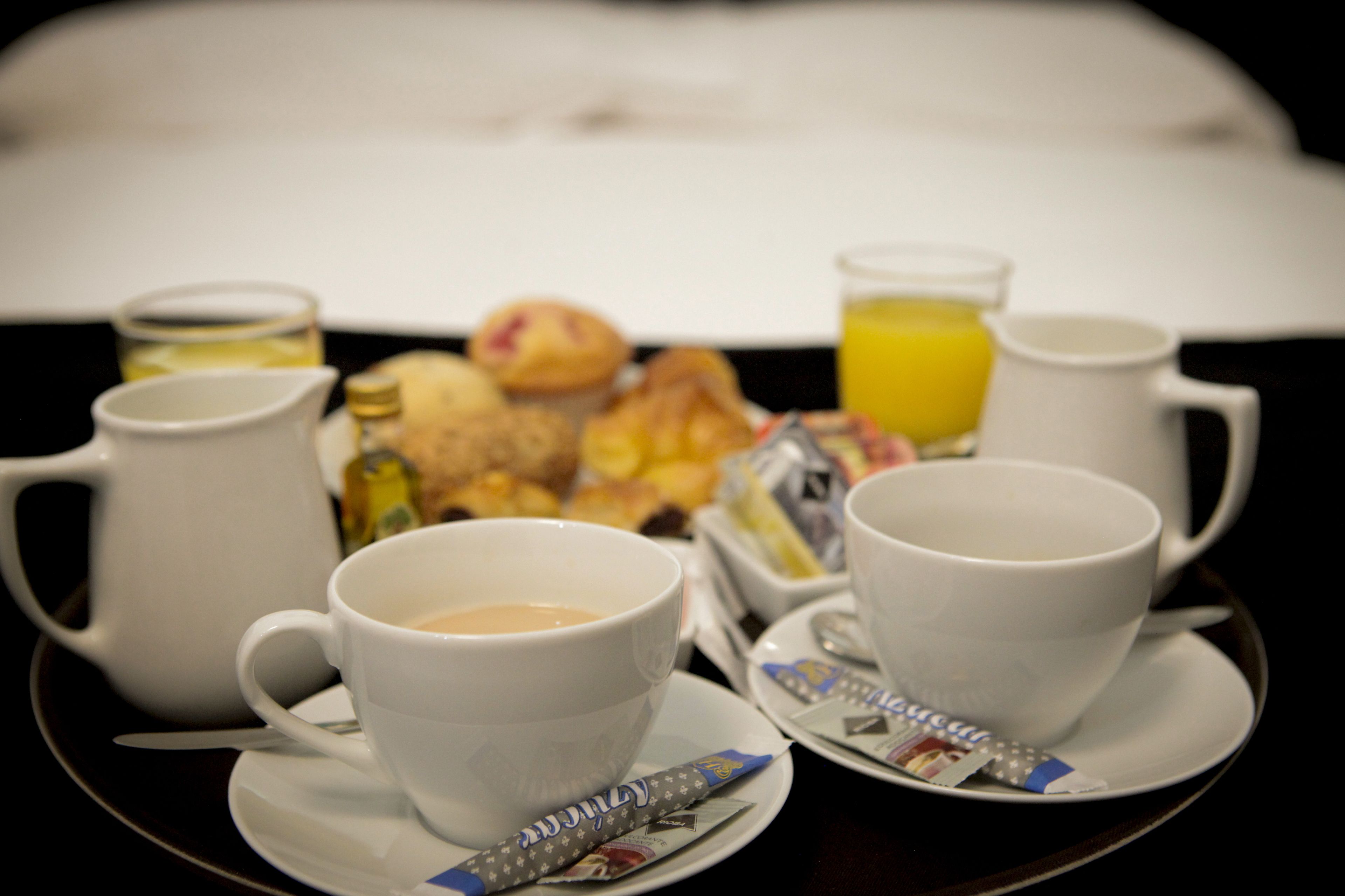 Une table mise pour le petit-déjeuner avec des tasses de café, un verre de jus d’orange et une assiette de viennoiseries.