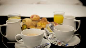 Une table mise pour le petit-déjeuner avec des tasses de café, un verre de jus d’orange et une assiette de viennoiseries.