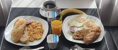 Egy asztalon tálalva: rántotta, pirítós, egy croissant, egy banán, egy csésze kávé és egy pohár narancslé – egy tipikus reggeli.
