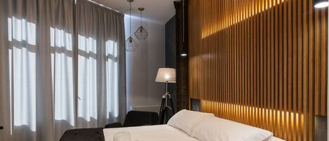 A modern bedroom with a wooden slatted wall, a bed with white linens, a black throw, and a wooden nightstand.